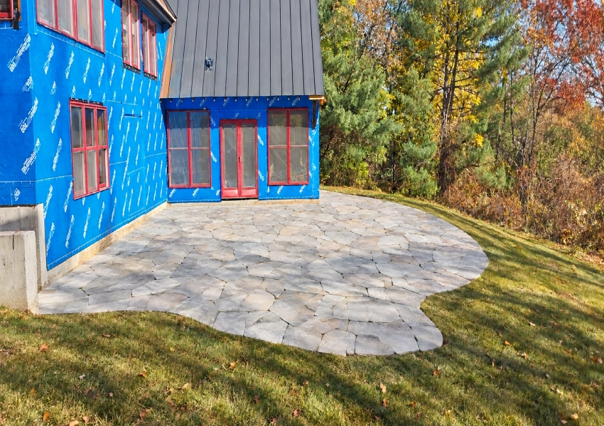 Finished natural stone patio with a curved edge and green lawn in Bolton Massachusetts M Coelho Group